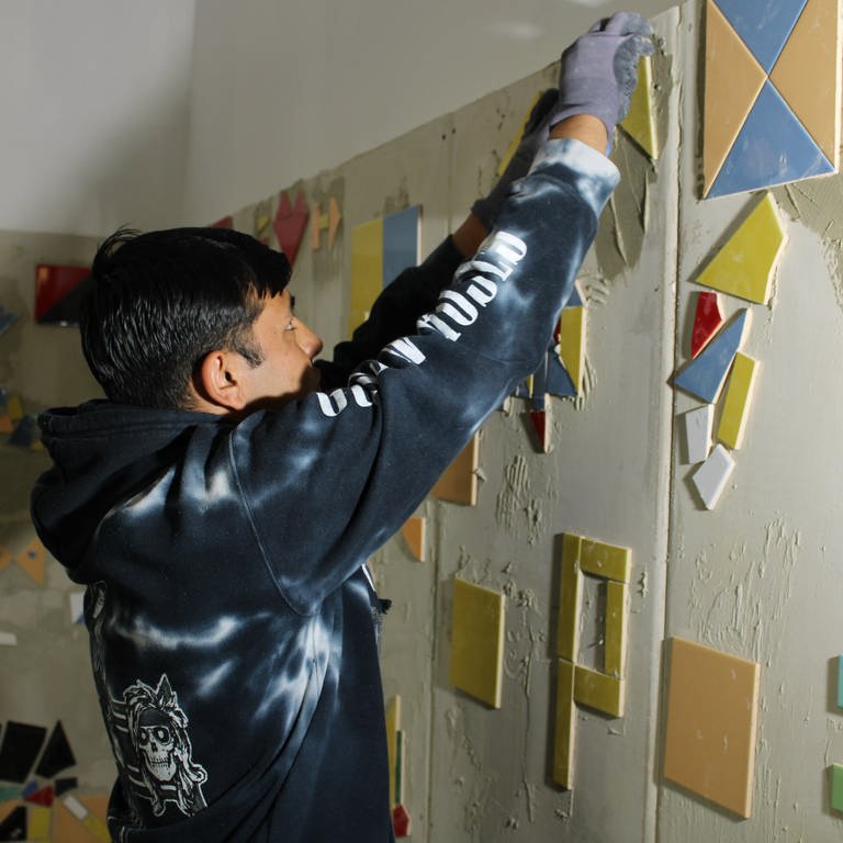 Ein Jugendlicher klebt im Makerspace in Mainz Fliesen an die Wand.