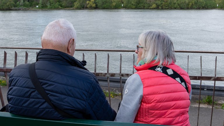 Zwei ältere Personen sitzen auf einer Bank mit dem Rücken zur Kamera.