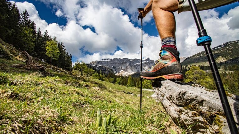 Wanderlust - Bein eines Wanderers, mit Bergschuh und Stöcken auf Stein im Gebirge