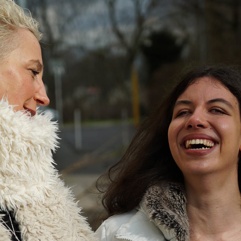 Mittelalte Frau lacht gemeinsam mit junger blinden Frau