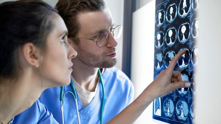 Eine Ärzt und ein Arzt schauen sich Röntgenbilder eines Schädels an