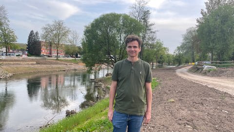 Projekteleiter Sebastian Krieg steht im unfertigen Flusspark Neckaraue. Im Hintergrund fließt der Neckar, am Ufer verlaufen erdige Wege.