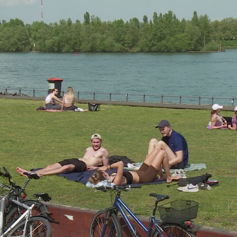 Menschen sonnen sich bei dem schönen Wetter am Rheinufer.