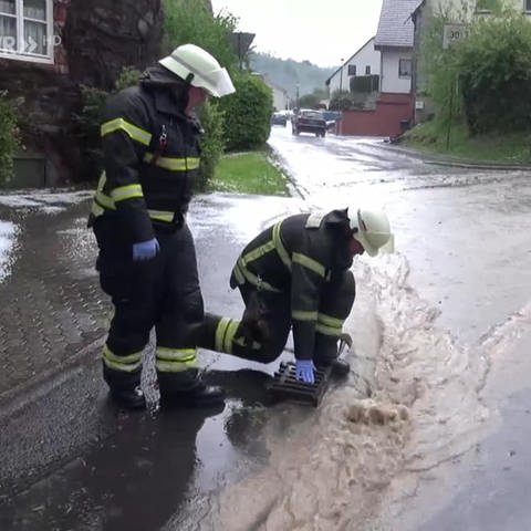 Zwei Feuerwehrmänner kümmern sich um den Gully in einer überfluteten Straße