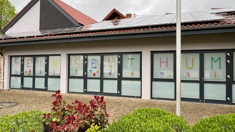 Bürgerhaus in Einselthum mit farbigem Schriftzug "Einselthum ist bunt" an den Fenstern.