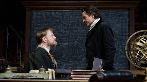 Professor Moriarty (Jared Harris) und Sherlock Holmes (Robert Downey Jr.) starren sich in einem Universitätssaal an.
