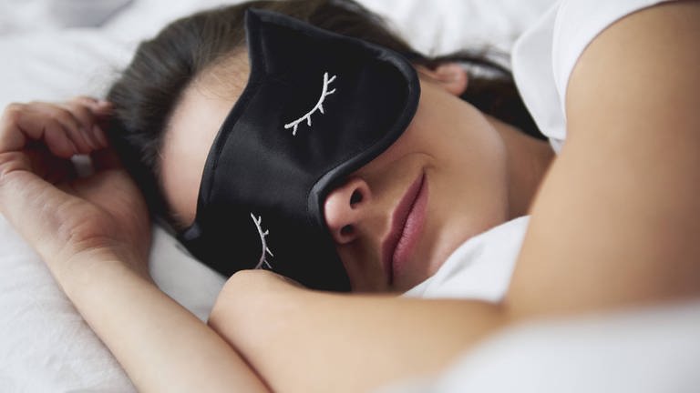 Junge Frau im Bett mit Schlafmaske 