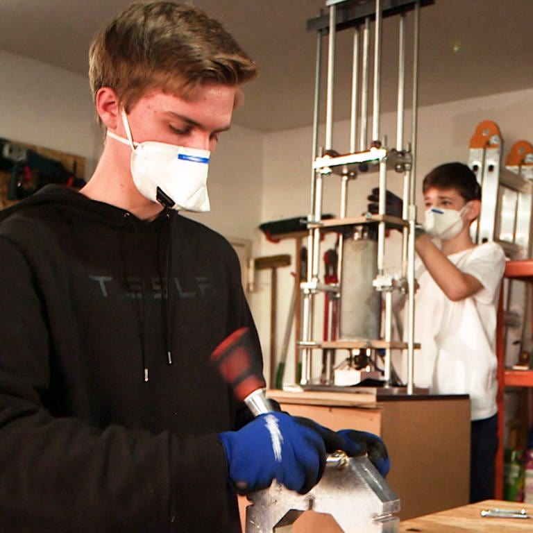 Zwei junge Schüler mit Atemmasken bauen an Maschinen aus Plastikmüll Schutzvisiere für Krankenhäuser