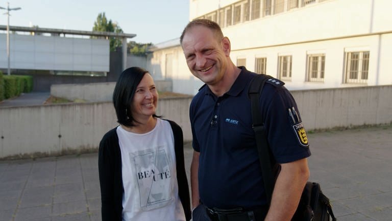 Mann in Uniform und Frau stehen im Gefängnis. Beide lächeln.