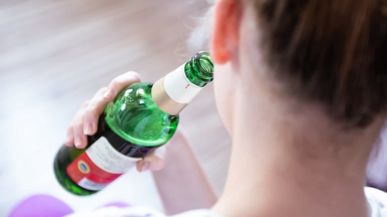 Alkoholsucht bei Jugendlichen: Ein Mädchen wurde von hinten fotografiert, wie sie aus einer Bierflasche trinkt 