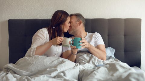 Ein Paar sitzt im Bett und küsst sich