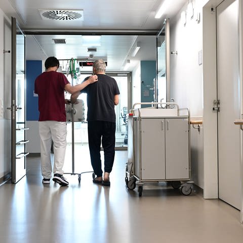 Ein Pfleger geht im Klinikum Stuttgart mit einem Patienten über einen Flur.