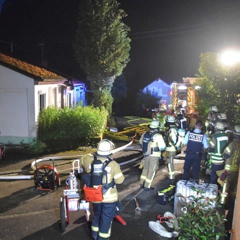 Einsatzkräfte von Feuerwehr und Polizei stehen am Abend um ein Haus.