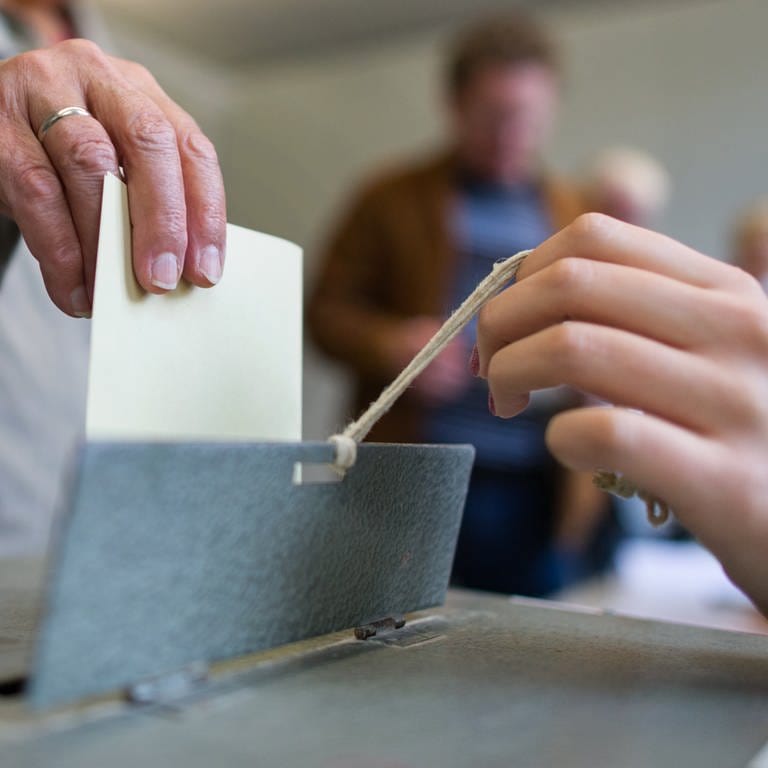 Hand wirft einen gelben Wahlzettel in eine Wahlurne. Am 14. März 2021 ist Landtagswahl in Rheinland-Pfalz 