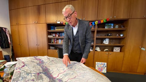 Bürgermeister Guido Orthen schaut auf einer Karte, wo die Starkregengefahren in Bad Neuenahr-Ahrweiler am größten sind. 
