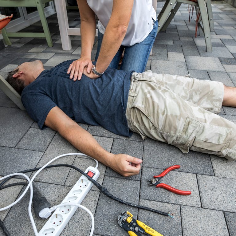Ein Mann liegt bewusstlos am Boden und wird mit Herz-Druck-Massage reanimiert.