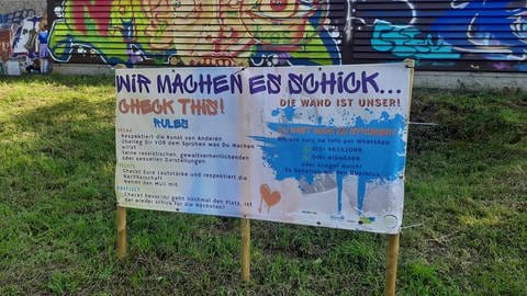 Vor dem mit Graffiti besprühten Oppenheimer Hallenbad steht ein Schild mit den Regeln für das Graffiti-Sprayen.