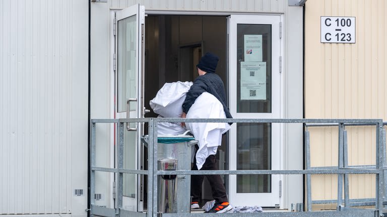Ein Mann geht mit Bettzeug in einen Container mit Wohnbereichen in der Aufnahmeeinrichtung für Asylbegehrende (AfA) in Trier.