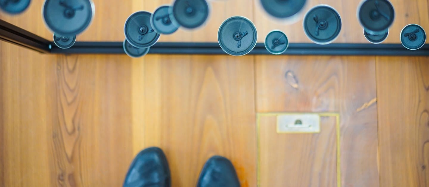 Donaueschinger Musiktage: Blick von oben auf schwebende Lautsprecher und schwarze Schuhe auf einem Holzboden
