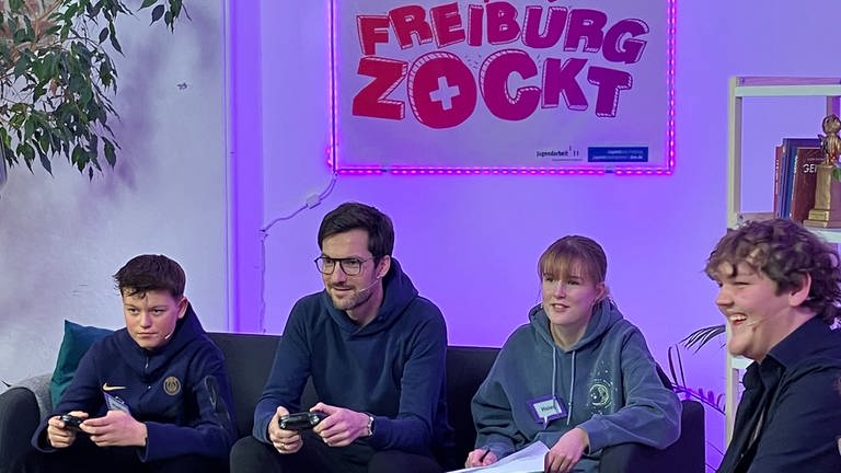 Freiburgs Oberbürgermeister Martin Horn spielt mit Jugendlichen ein Videospiel.