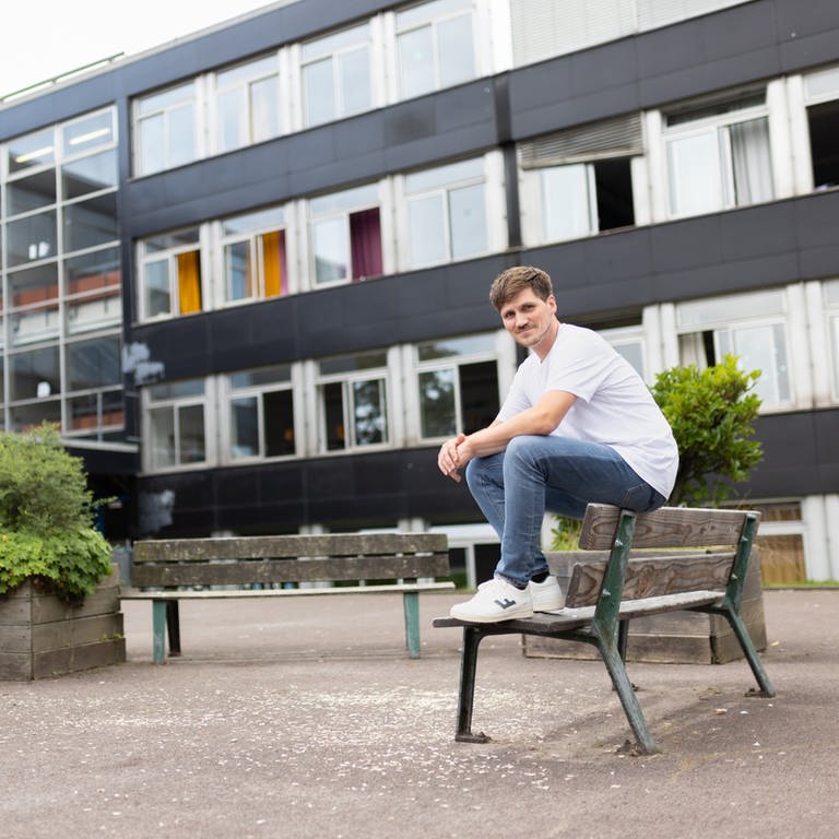Frank Seibert sitz auf einer Parkbank vor seiner Schule (Foto: SWR)