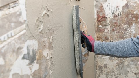 Ein Handwerker spachtelt eine Mauer mit Rissen und Unebenheiten zu
