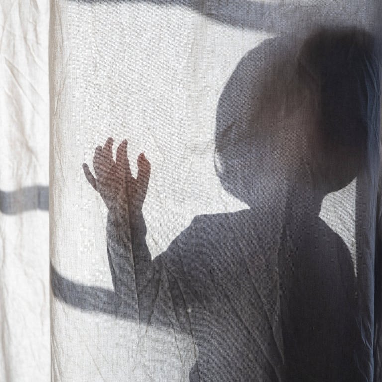 Schatten eines kleinen Kindes, das hinter einem Vorhang steht und die Hand hebt.