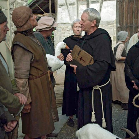 Auf einem Marktplatz steht eine Gruppe von Bauern drei Kleriker gegenüber. Die Kleriker tragen dunkle Kutten, einer von ihnen trägt eine Bibel.  (Foto: SWR, Jens Boeck)
