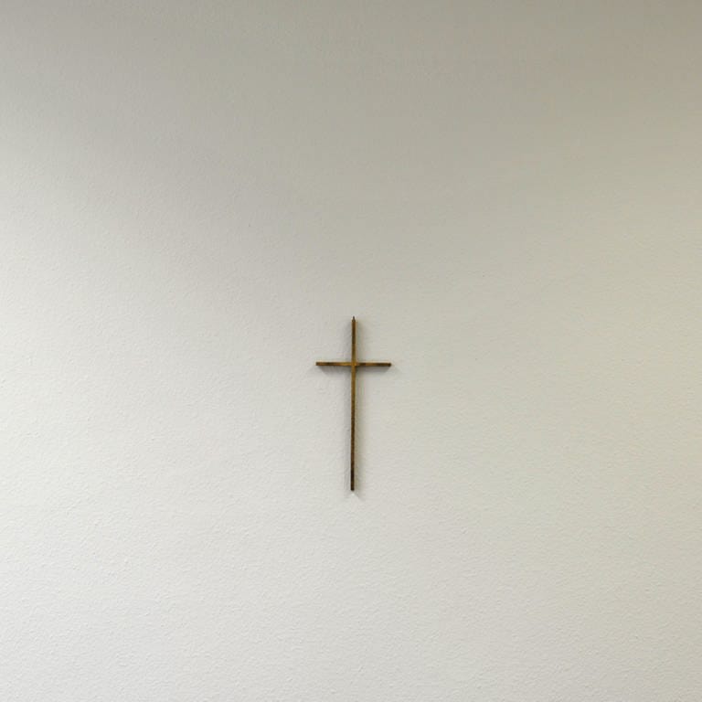 Ein christliches Kreuz hängt an einer weißen Wand. (Foto: dpa)