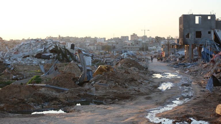 Menschen gehen vorbei an Trümmern und Ruinen auf einer Straße im Flüchtlingslager Al-Maghazi im Zentrum des Gazastreifens (Archivbild).  (Foto: dpa)