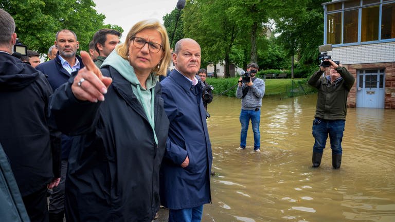 Rehlinger und Scholz stehen umringt von Medienvertretern auf einer überfluteten Straße in Kleinblittersdorf