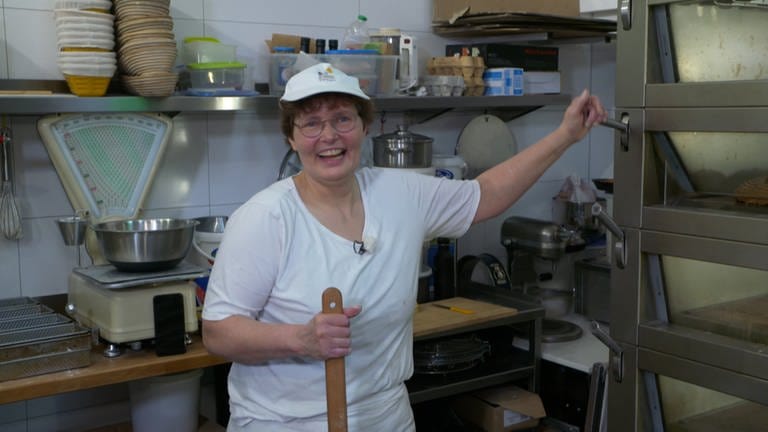 Frau mit Brille, kurzen Haaren und weißer Mütze und T-Shirt steht am Ofen in der Bäckerei (Foto: SWR)