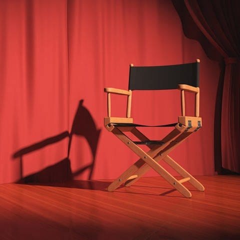 Ein Regiestuhl auf einer Bühne mit rotem Vorhang