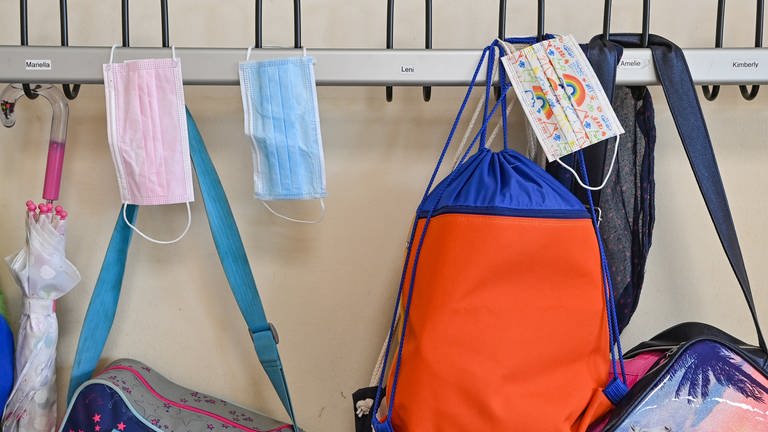Masken hängen zusammen mit Taschen und Rucksäcken an Kleiderhaken in einem Klassenraum einer Grundschule. (Foto: picture-alliance / Reportdienste, Picture Alliance)