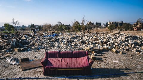 Im Vordergrund ein Sofa, im Hintergrund Steine von zerstörten Häusern