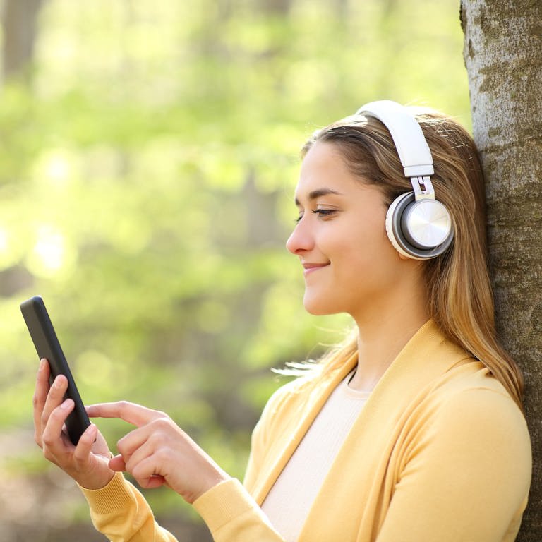 Junge Frau hört Musik über ihr Smartphone und hat Kopfhörer auf. (Foto: picture-alliance / Reportdienste, Picture Alliance)