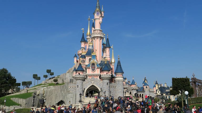 Besucher stürmen in Richtung Schloss in Disneyland Paris, ringsum blauer Himmel.