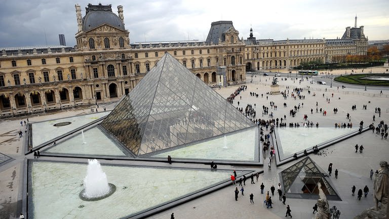 Touristen bewegen sich vor der Glaspyramide im Innenhof des Louvre in Paris.