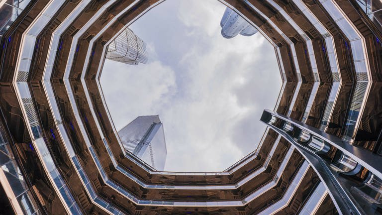 Betrachter steht in der Mitte des Treppenturms The Vessel in New York. In der Mitte ist der Himmel zu sehen.