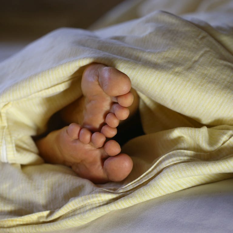 Die Füße einer Frau ragen unter einer Bettdecke hervor