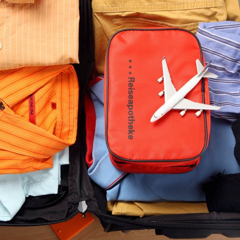 Eine Tasche mit der Aufschrift Reiseapothke liegt in einem gepackten Koffer. Auf ihr befindet sich ein kleines Flugzeug (Foto: picture-alliance / Reportdienste, Picture Alliance)