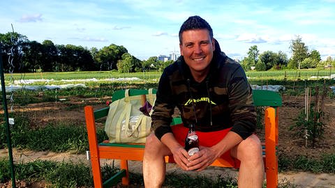SWR4 Team: Andreas Dangel auf einer roten Bank am Gemüseacker.