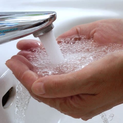 Tipps fürs Wasser sparen im Alltag: Zwei Hände werden in einem Waschbecken unter fließendes Wasser gehalten.
