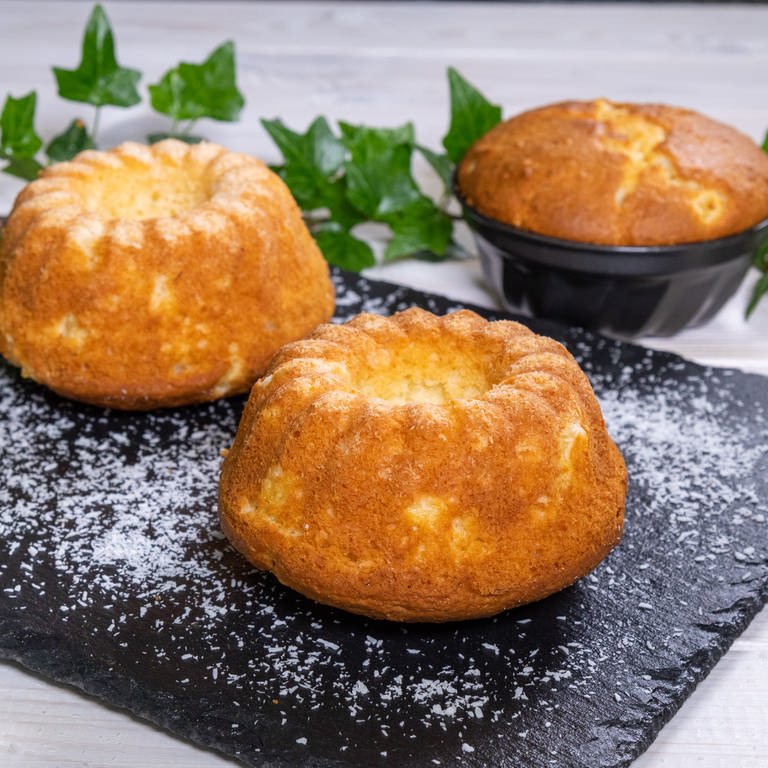 Leckeres Rezept für Ananas-Kokos-Cake: drei kleine Kuchen serviert auf einer dunklen Steinplatte. Ein Küchlein ist noch in einer schwarzen Form.