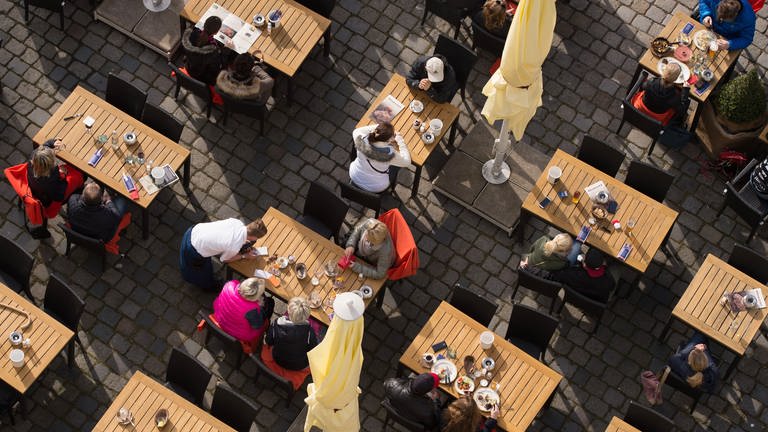 Foto aus der Vogelperspektive: Gäste sitzen in einem Straßencafe in der Sonne