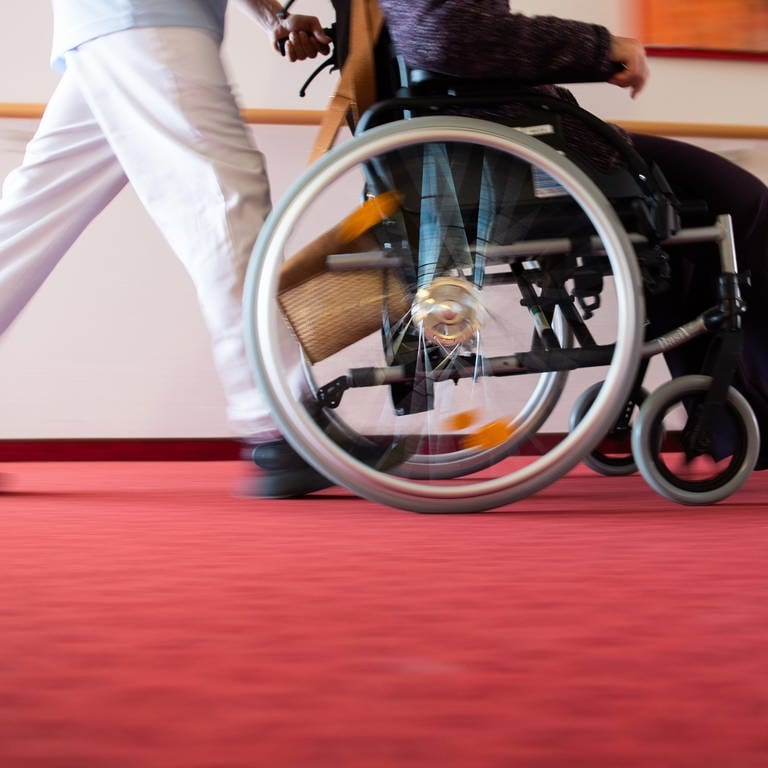 Ein Pfleger eines Pflegeheims schiebt eine Bewohnerin mit einem Rollstuhl.