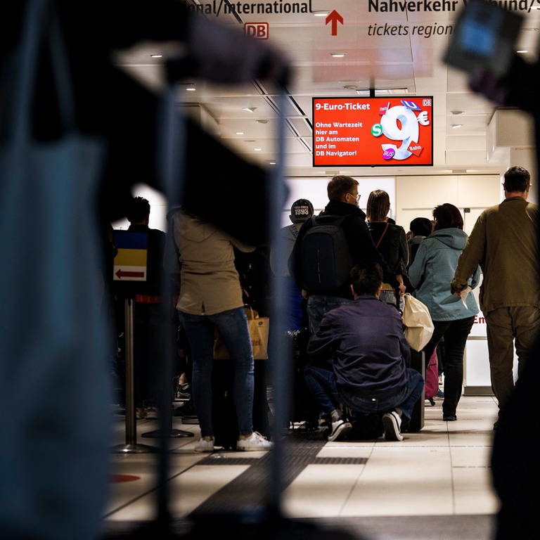 Kunden stehen in einer Schlange unter einem Hinweißschild für das 9-Euro-Ticket im Reisezentrum der Deutschen Bahn im Berliner Hauptbahnhof.