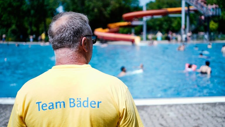 Ein Schwimmmeister steht im Herzogenriedbad in Mannheim vor einem Schwimmbecken mit Wasserrutsche.