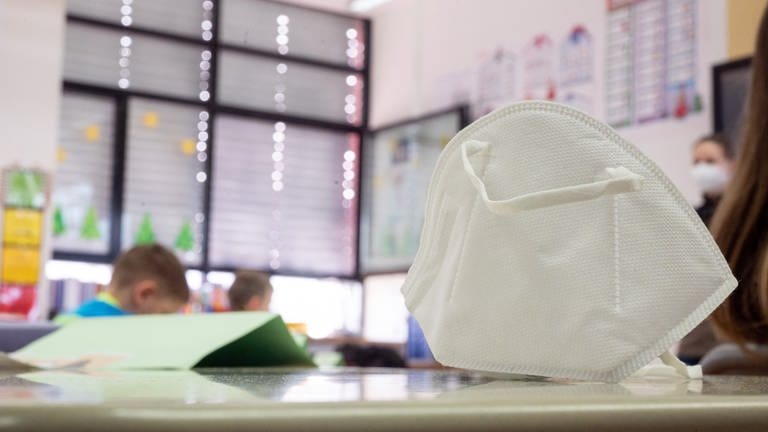 Eine FFP2-Maske liegt in einer ersten Klasse an einer Grundschule. Baden-Württemberg lockert die Regeln zur Eindämmung des Coronavirus an Schulen - Schwangere Lehrerinnen dürfen länger eine FFP2-Maske tragen