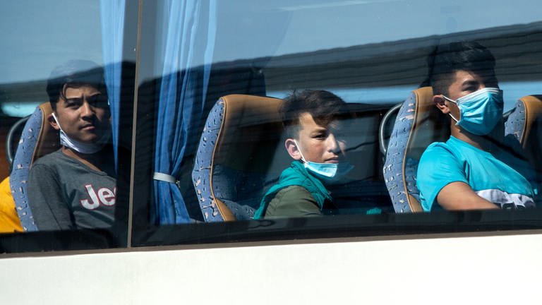 Junge Flüchtlinge, teilweise mit Mundschutz, sitzen in einem Bus